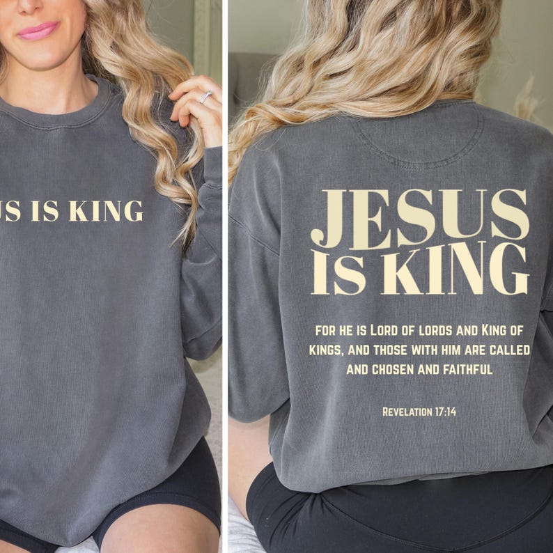 May include: A charcoal gray sweatshirt with the text "JESUS IS KING" printed in a cream color on the front and back. The back also features a Bible verse. A comfortable, casual top.