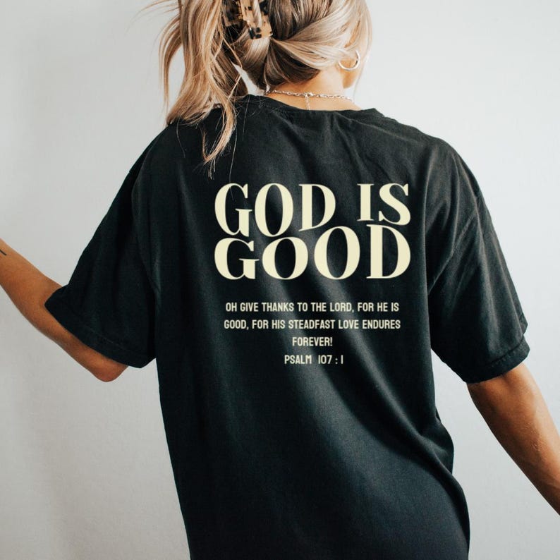 May include: Black t-shirt with the text "GOD IS GOOD" in a cream color. The text "OH GIVE THANKS TO THE LORD, FOR HE IS GOOD, FOR HIS STEADFAST LOVE ENDURES FOREVER! PSALM 107:1" is printed below in a smaller font.