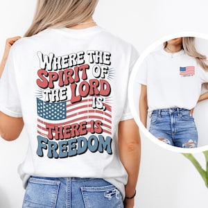 May include: White t-shirt with a patriotic design. The back of the shirt features the text "Where the Spirit of the Lord Is, There Is Freedom" above an American flag graphic. A smaller American flag is on the front.