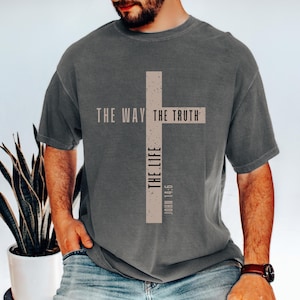 May include: Grey t-shirt featuring a tan cross design. The cross includes the words "THE WAY THE TRUTH THE LIFE" and "JOHN 14:6". The shirt is short-sleeved and has a crew neck.
