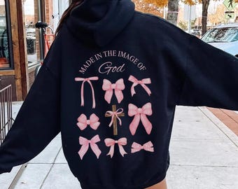 May include: Black hooded sweatshirt with the text "Made in the Image of God" and pink bows printed on the back.
