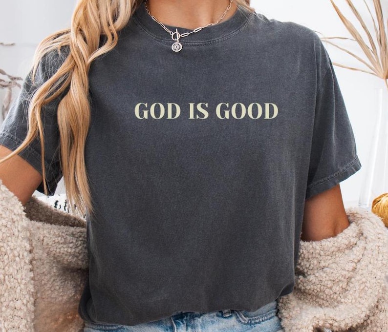 May include: A dark gray cropped t-shirt with the text "GOD IS GOOD" in white lettering.
