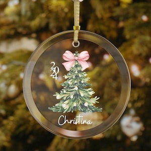 May include: Clear glass Christmas bauble with a gold ribbon. The bauble features a watercolour Christmas tree with a pink bow, the year 2024, and the name "Christina" in a script font.