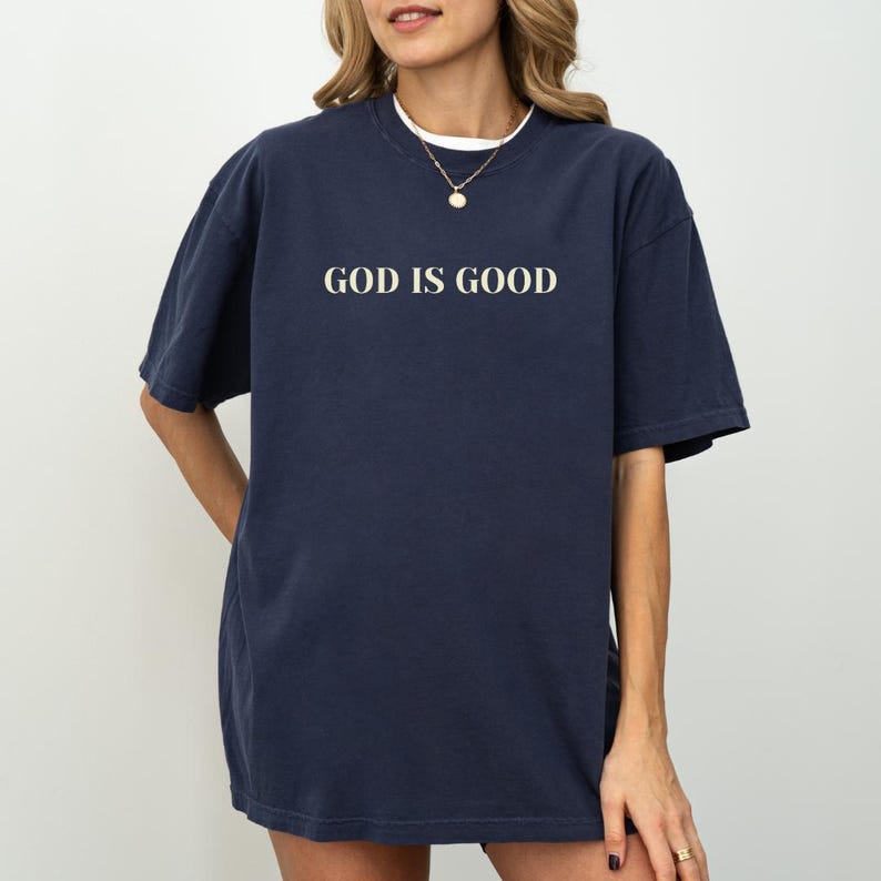 May include: A navy blue oversized t-shirt with the text "GOD IS GOOD" printed in white on the front.