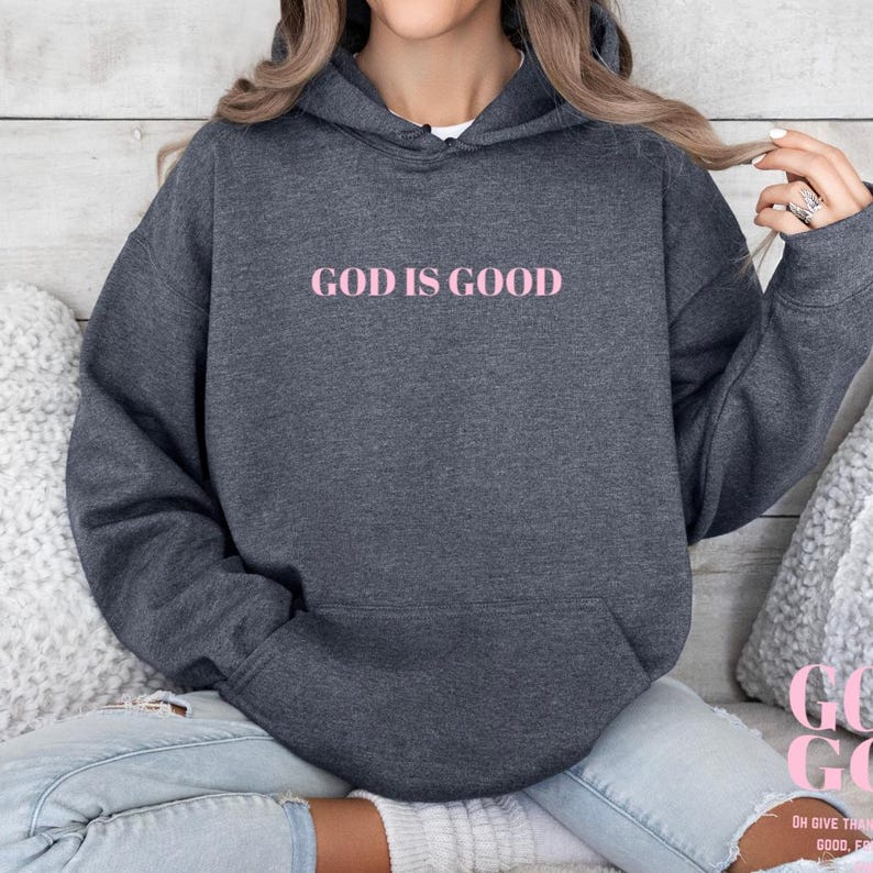 May include: A dark gray hooded sweatshirt with the text "GOD IS GOOD" printed in pink on the front.