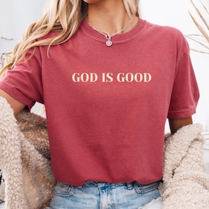 May include: A red t-shirt with the text "GOD IS GOOD" printed in a cream color on the front.