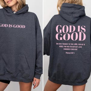 May include: A dark gray hooded sweatshirt with the phrase "God is Good" printed in pink on the front and back. The back also includes the text "Oh give thanks to the Lord, for he is good, for his steadfast love endures forever! Psalm 107:1."
