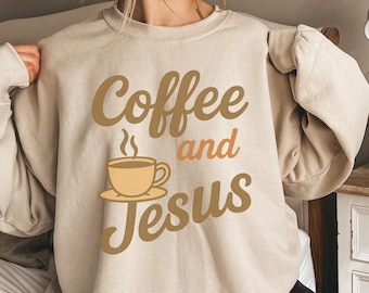 May include: Beige sweatshirt with the words "Coffee and Jesus" in brown and orange lettering. A steaming coffee cup graphic is featured below "Coffee". The sweatshirt is a neutral colour and has long sleeves.
