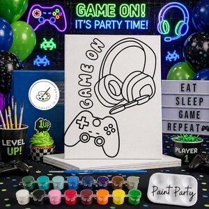 May include: A paint party kit with a canvas featuring a controller and headset design, along with paint pots in various colors. The words "GAME ON!" and "IT'S PARTY TIME!" are displayed. Balloons and a cupcake are also visible.