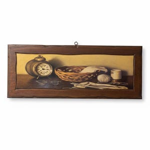 Puede incluir: Una pintura de naturaleza muerta con un despertador de latón, gafas, una cesta tejida con tela, una madeja de lana, una taza blanca pequeña y agujas de tejer. La pintura está enmarcada en un marco de madera marrón oscuro.
