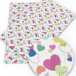 May include: A sheet of white faux leather with a repeating pattern of colourful hearts. The hearts are in various shades of pink, blue, green, and yellow. The hearts are outlined in black and have a white background.