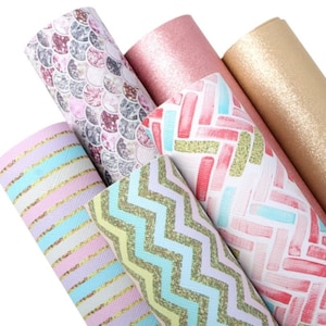 May include: Five different patterned faux leather sheets. The sheets feature a pink and gray mermaid scale pattern, a pink and white chevron pattern, a pink and white brick pattern, a pink glitter sheet, and a gold glitter sheet.