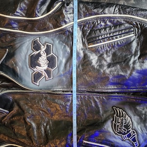 May include: A black leather jacket with white piping, featuring embroidered patches including the text 'Avirex' and '75'. A blue measuring tape is placed vertically over the center, showing a length of approximately 27 inches from the top to the hem.