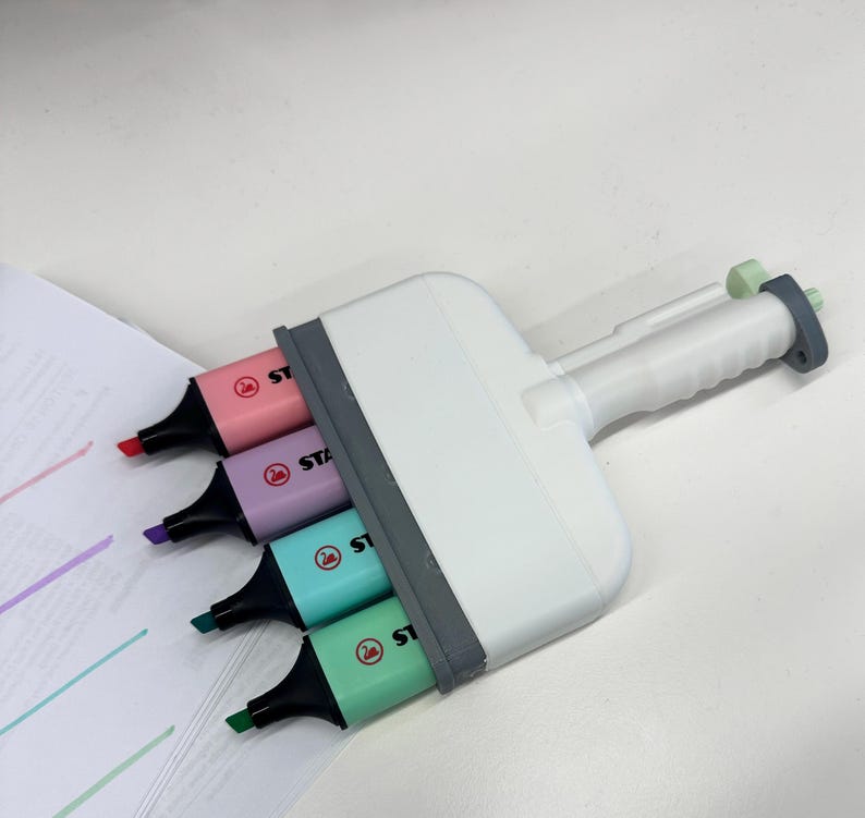 Puede incluir: Una herramienta resaltadora m&uacute;ltiple de pl&aacute;stico blanco con cuatro marcadores Stabilo integrados en tonos pastel rosa, morado, turquesa y verde claro. El dispositivo tiene un marco gris y un mango texturizado, con las puntas alineadas para trazar l&iacute;neas.