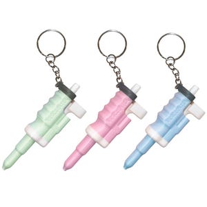 May include: Three colorful keychains in pastel shades of green, pink, and blue. Each keychain features a small, detailed design with a silver keyring and chain. The text "Vescienza" is visible on each keychain.