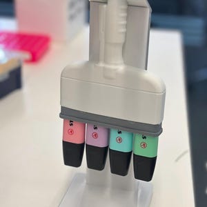Puede incluir: Un soporte organizador de escritorio de pl&aacute;stico blanco que sostiene cuatro resaltadores de colores pastel en rosa, morado, turquesa y verde claro. Cada resaltador tiene una tapa negra y un cuerpo blanco con la letra S impresa en el lateral.