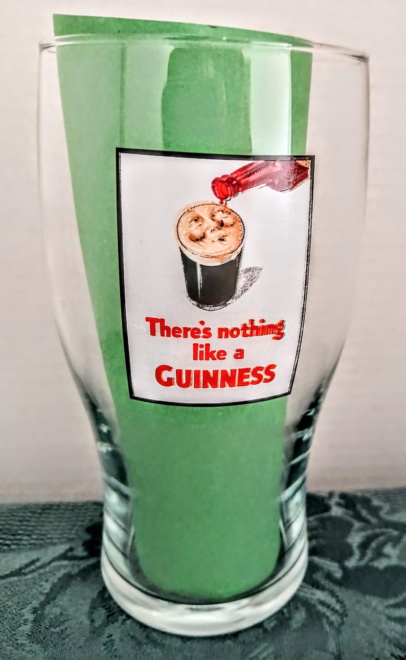 Może przedstawiać: Przezroczysty szklany kufel z zieloną wkładką. Na szkle grafika przedstawiająca nalewane piwo Guinness z czerwonym napisem "There's nothing like a GUINNESS".