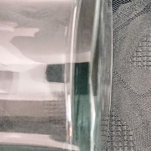 Może przedstawiać: Przezroczysty, szklany, cylindryczny przedmiot z zaokrągloną podstawą. Szkło ma lekki zielonkawy odcień i jest częściowo wypełnione białą substancją. Przedmiot jest umieszczony na teksturowanym szarym tle.