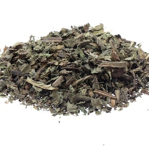 May include: A pile of dried, chopped herbs against a white background. The herbs are primarily green and brown, with a slightly coarse texture. The image is well-lit, highlighting the details of the dried leaves and stems.