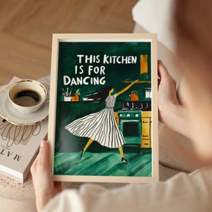 Puede incluir: Una impresión enmarcada con un fondo verde y una mujer bailando en una cocina. El texto en la impresión dice "This kitchen is for dancing."