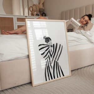 以下が含まれることがあります： 縞模様のドレスを着た人物の白黒のイラスト。イラストは明るい木製のフレームで囲まれています。