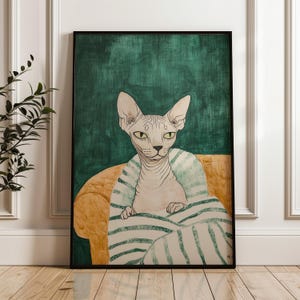 May include: Framed art print featuring a Sphynx cat seated on a yellow sofa, wrapped in a striped blanket. The cat has pale skin and green eyes, set against a dark green background. The artwork is in a black frame.