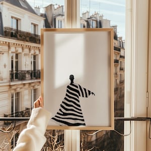 Peut inclure: Une illustration en noir et blanc d'une personne portant une robe rayée. L'illustration est encadrée dans un cadre en bois clair.