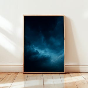 Peut inclure: Impression encadrée représentant un orage. Le ciel est dominé par des nuages bleu foncé et noirs, traversés par des éclairs. Le cadre en bois met en valeur l'œuvre, accrochée sur un mur blanc et posée sur un parquet.