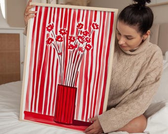 May include: A framed art print featuring a red and white striped background with a red vase holding red flowers. The artwork has a light wooden frame. The overall theme is floral and decorative.