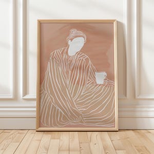 以下が含まれることがあります： 線画で描かれた、カップを持った人が座っているデジタルアートプリント。人物はストライプのローブを着ており、背景はソフトなピーチカラーです。