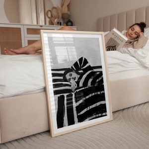 以下が含まれることがあります： 縞模様の表面に横たわる人物の白黒イラスト。イラストは明るい木製のフレームに収められ、白いベッドに寄りかかっている。