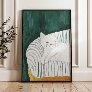 Pode incluir: Uma impressão de arte emoldurada com um gato branco dormindo pacificamente em uma almofada listrada. O gato está em um fundo verde escuro, com a almofada em um padrão listrado amarelo claro e branco. A obra de arte está em uma moldura preta.
