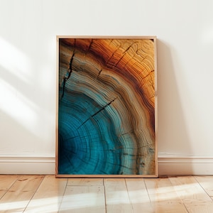 Op de afbeelding: Een ingelijste print met een close-up van een boomdoorsnede. Het kunstwerk toont concentrische ringen in tinten blauw, oranje en bruin, met zichtbare scheuren en een natuurlijke houtnerftextuur. De lijst heeft een lichtbruine kleur.