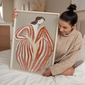 以下が含まれることがあります： 赤と白のストライプの服を着た人物の額縁入りイラスト。人物は腕を組み、頭を横に傾けて立っている。背景は薄いグレーです。