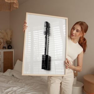 Op de afbeelding: Een zwarte mascara-applicator op een witte achtergrond. De mascara-applicator zit in een doorzichtige buis met een zwarte dop.