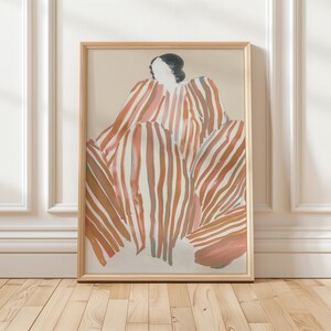 以下が含まれることがあります： 縞模様の服を着た人物の抽象画が額装されています。縞模様はピンク、オレンジ、ブラウンの色合いです。背景は薄いベージュです。