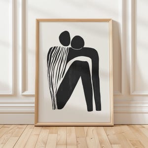 Könnte beinhalten: Schwarz-weißes abstraktes Kunstprint von zwei sich umarmenden Figuren. Der Druck ist in einem hellen Holzrahmen gerahmt.