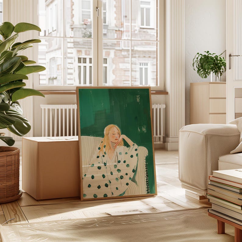May include: A framed art print featuring a woman with blonde hair in a white and green polka dot robe, resting on a white sofa. The background is a vibrant green with a wooden frame. The artwork is displayed in a bright, airy room.