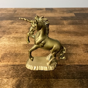 May include: A golden brass unicorn figurine, rearing up on its hind legs. The mythical creature has a detailed mane, tail, and horn. The unicorn is mounted on a small, textured base, ideal for home decor or a collector's item.