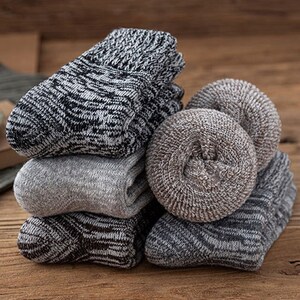 May include: A stack of five pairs of socks in various shades of grey and brown. The socks are made of a soft, knitted fabric and have a textured pattern.