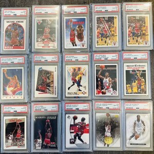 May include: A collection of 12 Michael Jordan basketball trading cards in protective plastic cases. The cards feature various images of Jordan playing basketball, including a card with the text "NBA Hoops Tribune Jordan Bulls Win First Title".