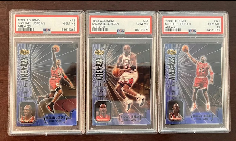 May include: Three graded trading cards featuring Michael Jordan, each card is in a protective case and graded as Gem Mint 10. The cards are from the 1998 U.D. Ionix Area 23 series.