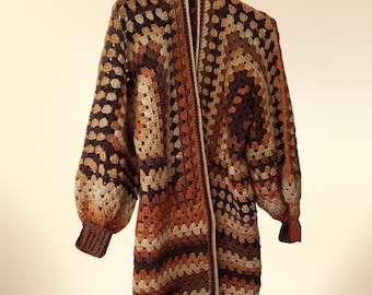 Könnte beinhalten: Ein langer, brauner, orangefarbener und beiger Häkelcardigan mit geometrischem Muster. Der Cardigan hat einen Schalkragen und lange Ärmel.