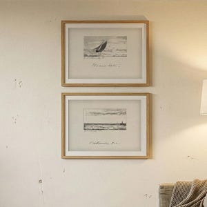 May include: A cozy living room scene with two framed nautical prints, a wooden coffee table, and a sofa with pillows and a blanket. A floor lamp with a beige shade provides warm lighting. A potted plant adds a touch of nature.