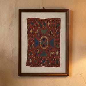 May include: A brown ceramic pitcher filled with a bouquet of dried wildflowers, including daisies and wheat stalks, sits next to a stack of three beige books and a framed textile wall hanging featuring a red, blue, and yellow geometric pattern.