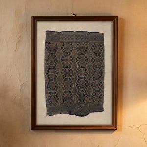 May include: A brown ceramic pitcher filled with a bouquet of dried wildflowers, including yellow, white, and purple blossoms, alongside a framed rectangular textile piece featuring a dark blue and grey geometric pattern on a light background.