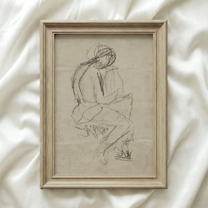 Könnte beinhalten: Eine gerahmte Kohleskizze einer sitzenden Figur, die in lockeren, ausdrucksstarken Linien dargestellt ist. Das Kunstwerk wird in einem hellen Holzrahmen vor einem weichen, cremefarbenen Hintergrund präsentiert. Die Skizze fängt die Form einer Person in einer nachdenklichen Pose ein.