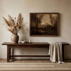 May include: A dark brown wooden bench with a beige throw blanket draped over one end. On the bench sits a large tan ceramic vase filled with dried pampas grass and seed pods, a small bowl, and a candle. A framed landscape painting hangs above.