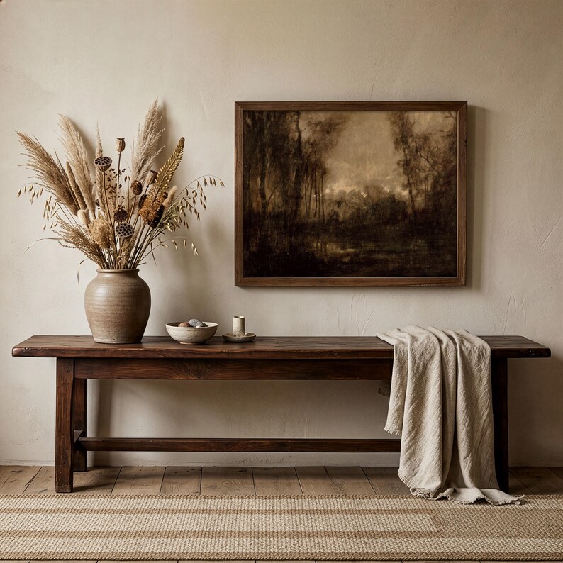May include: A dark brown wooden bench with a beige throw blanket draped over one end. On the bench sits a large tan ceramic vase filled with dried pampas grass and seed pods, a small bowl, and a candle. A framed landscape painting hangs above.