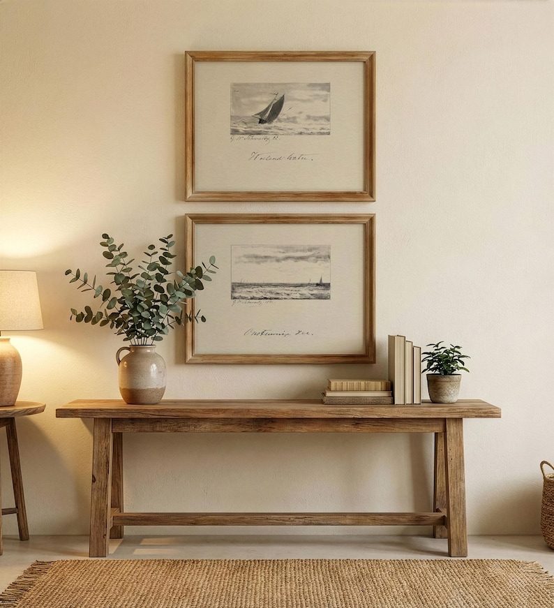 May include: Two framed nautical prints featuring sailboats are displayed above a wooden console table. The table is adorned with a vase of greenery, books, and a potted plant. A jute rug and a lamp complete the scene.